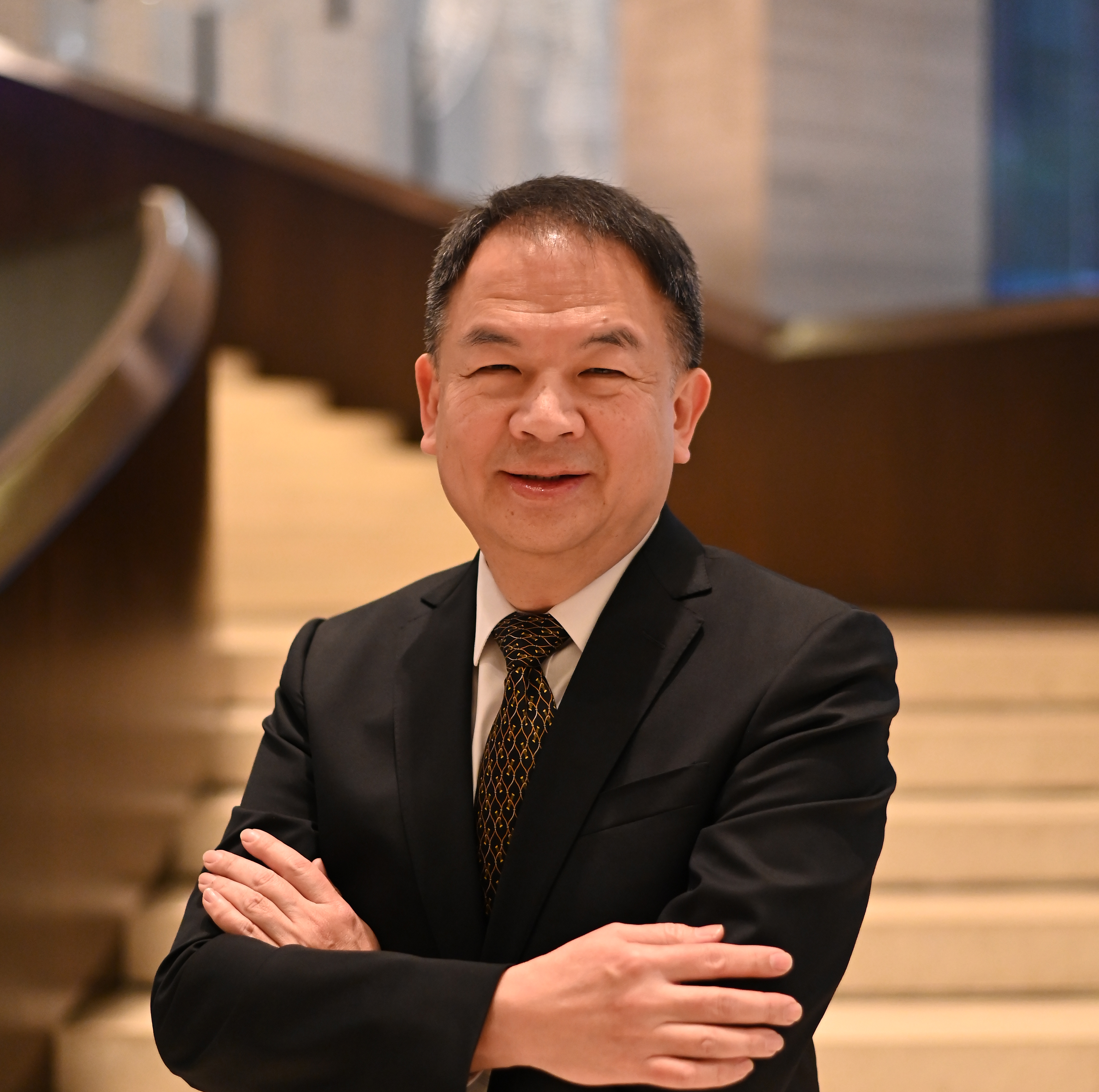 A man in a suit stands with arms crossed on a staircase in a modern interior.