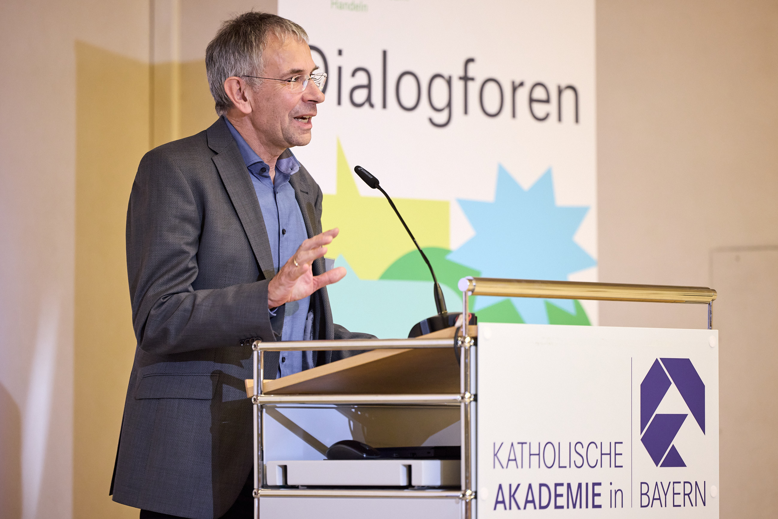 Ein Mann spricht an einem Rednerpult vor einem Banner der Katholischen Akademie in Bayern.