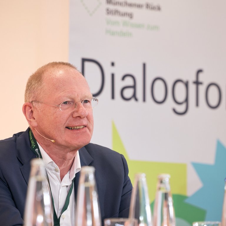 Zwei Personen sitzen an einem Tisch, im Hintergrund ein Banner mit dem Text "Dialogforen".