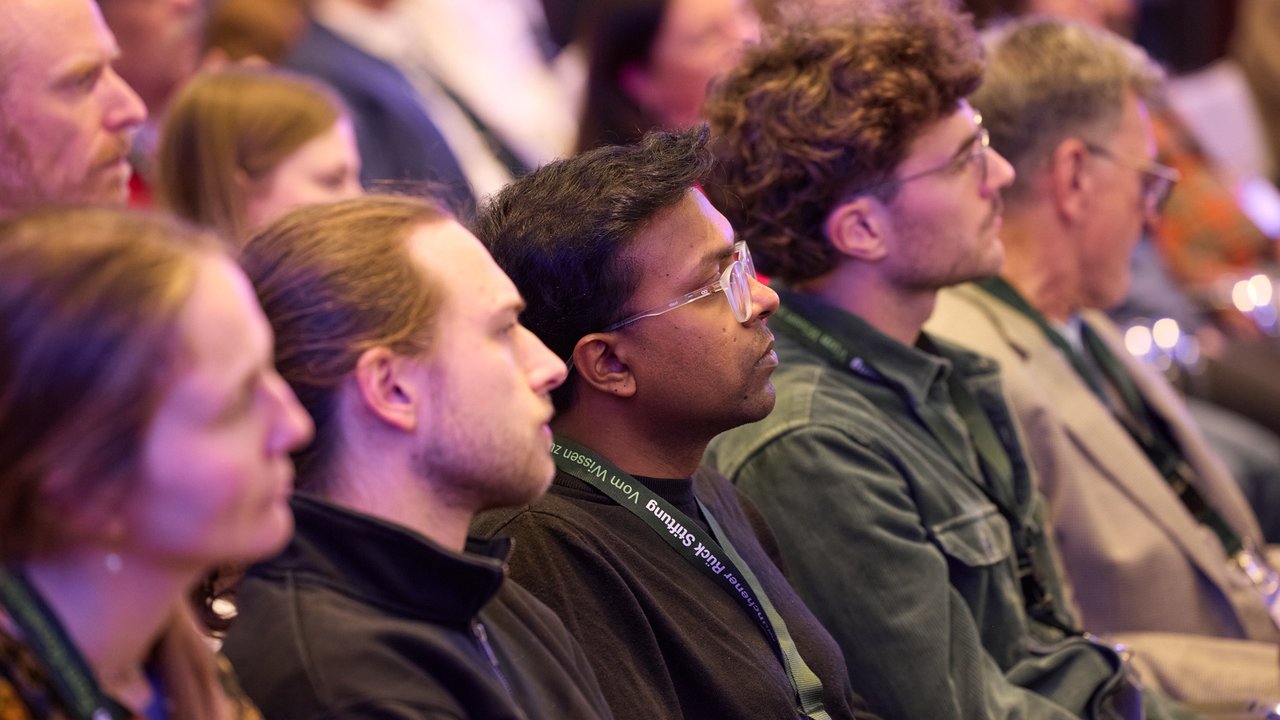 A group of people sitting in an audience, mostly facing forward, with blurred faces for privacy.