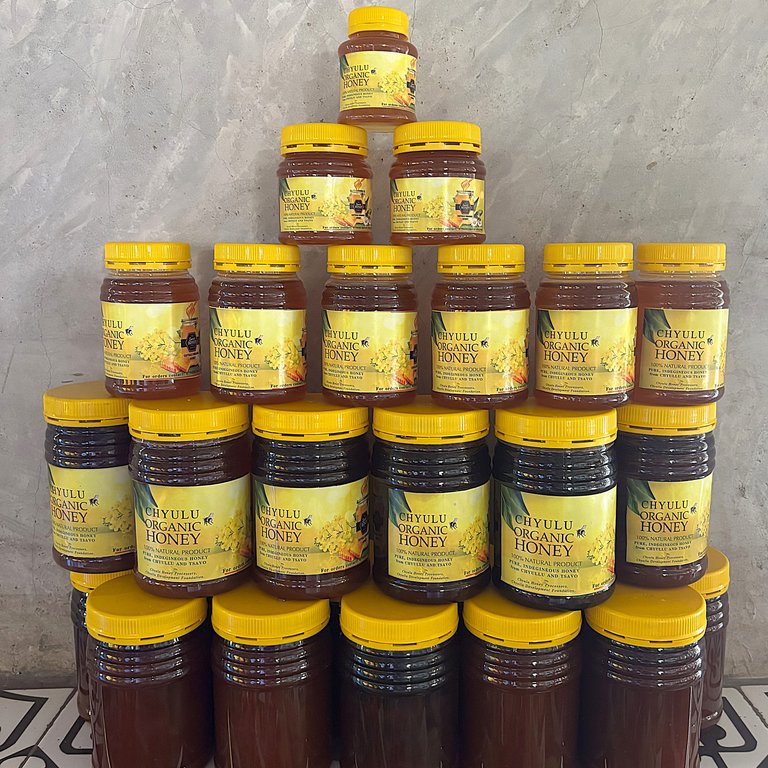 A pyramid of jars filled with organic honey, labeled with yellow lids and a floral design, on a textured background.