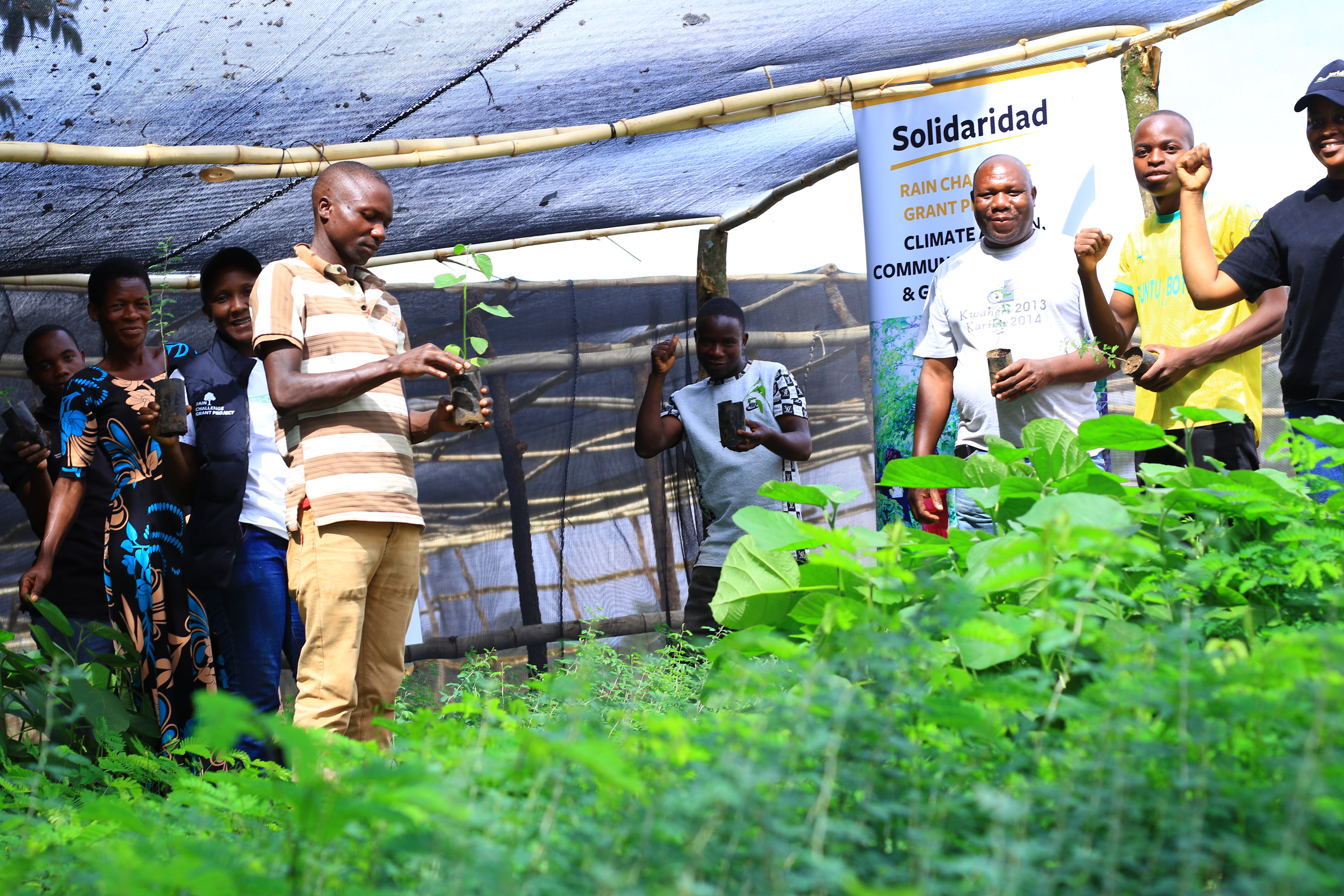 A group of people holding young plants in a greenhouse with greenery around them.