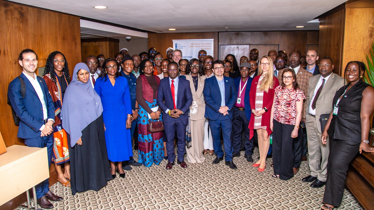 A group of diverse individuals stands together in a conference room, with wooden walls and a patterned carpet.