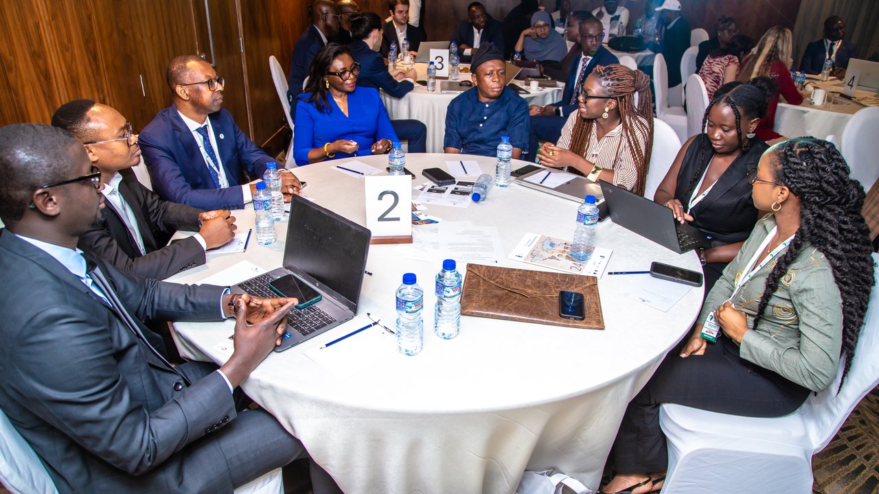 A group of people seated around a table with laptops, water bottles, and papers in a conference setting.