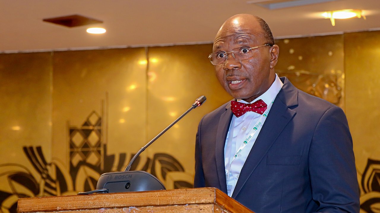 A man in a suit speaks at a podium with a microphone, set against a decorative background.