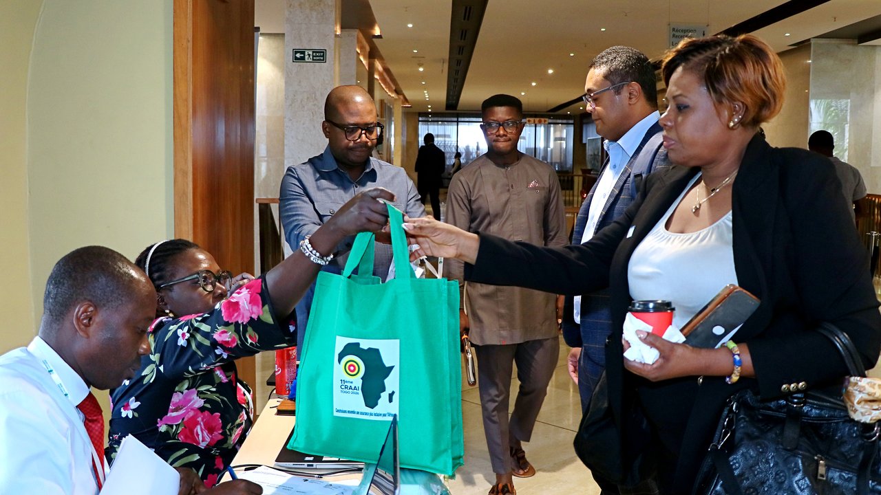 A group of people at a reception area exchanging items, including a green tote bag with a logo.
