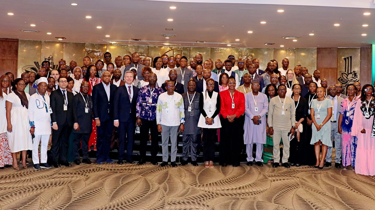 A large group of people poses for a photo at an event, with a decorated background and screens displaying information.