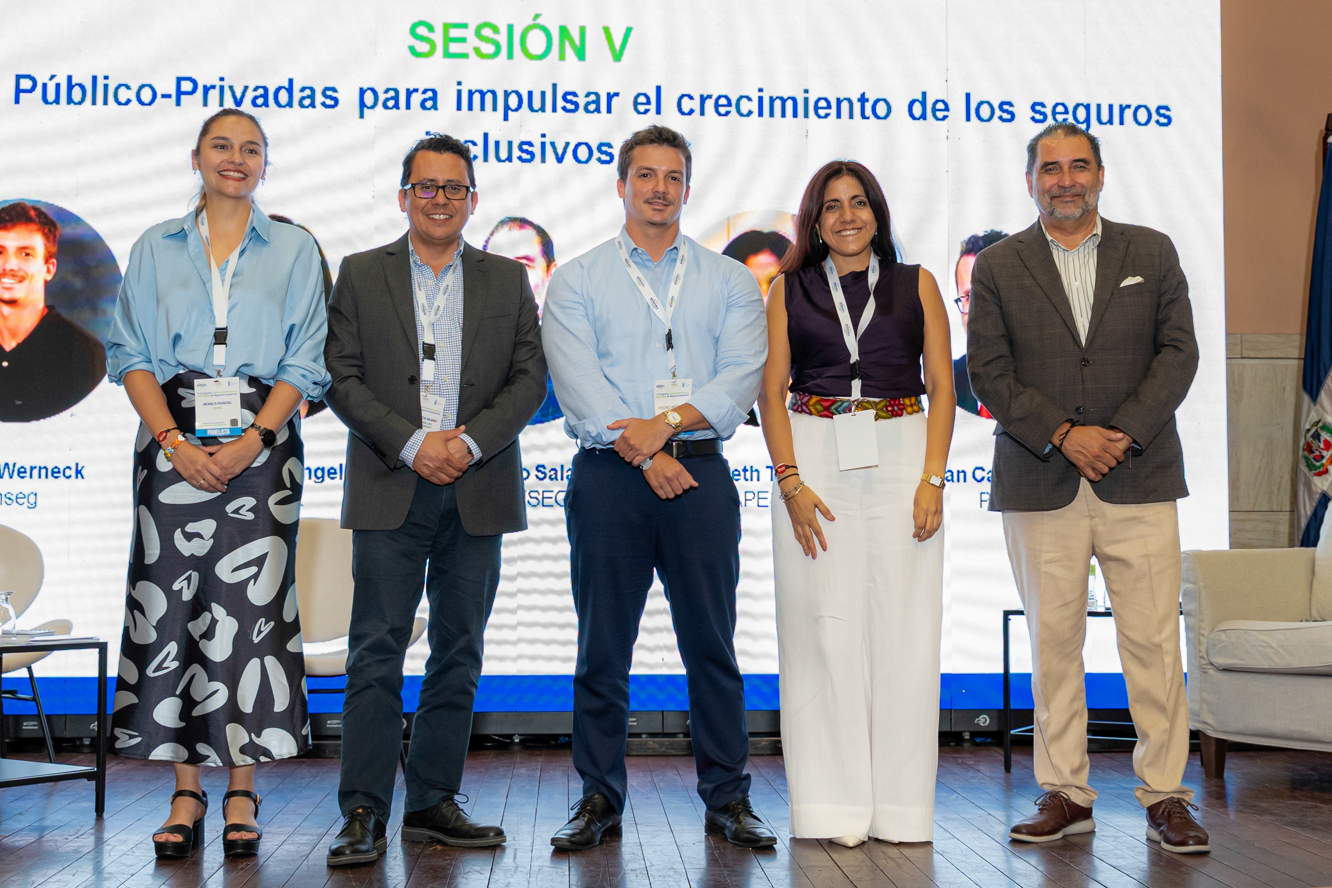 Cinco personas de pie en un escenario, con un fondo que muestra el título de una sesión sobre seguros inclusivos.