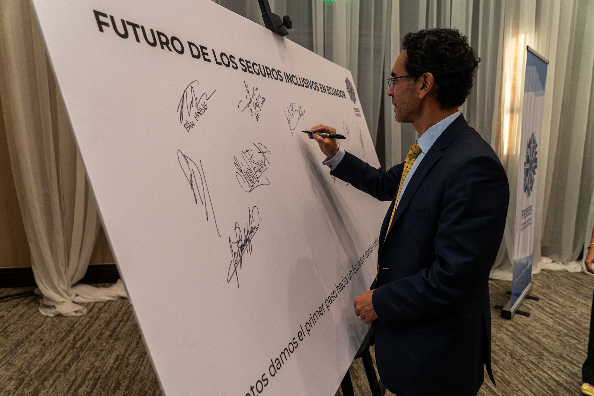 A person signs a large white board with multiple signatures