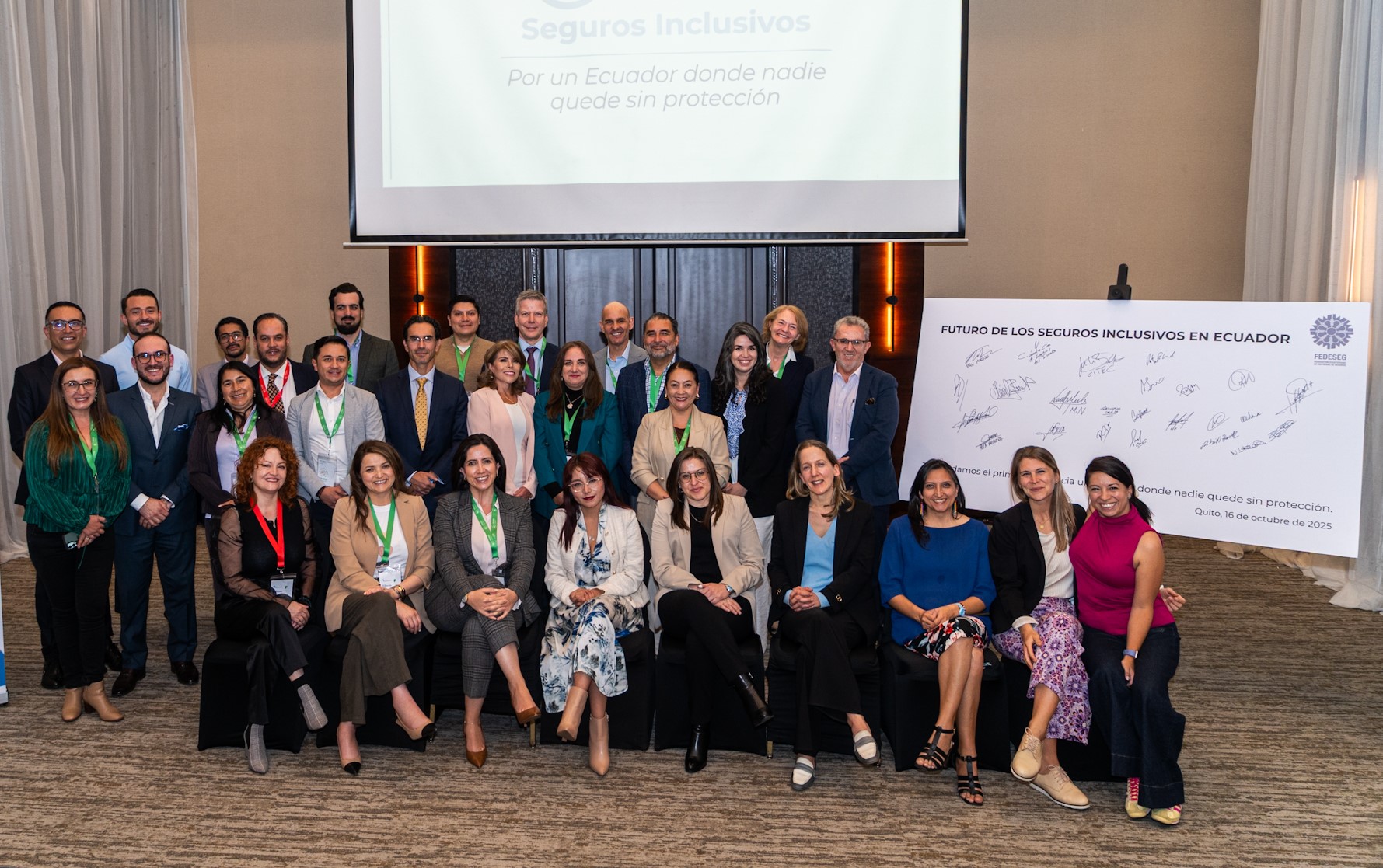 Group photo at an event, with a declaration on inclusive insurance in Ecuador in the background