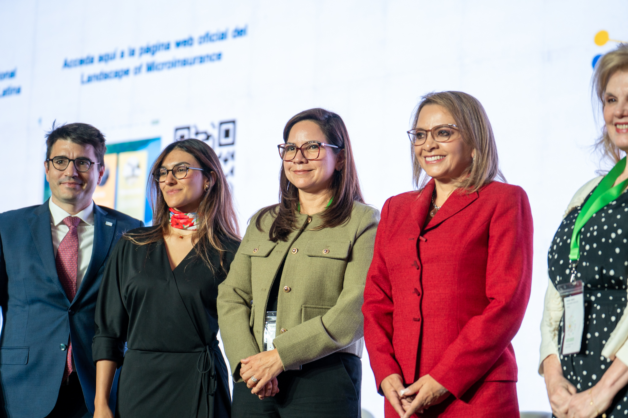 Five people pose for a photo at an event, with a presentation screen and a visible QR code in the background