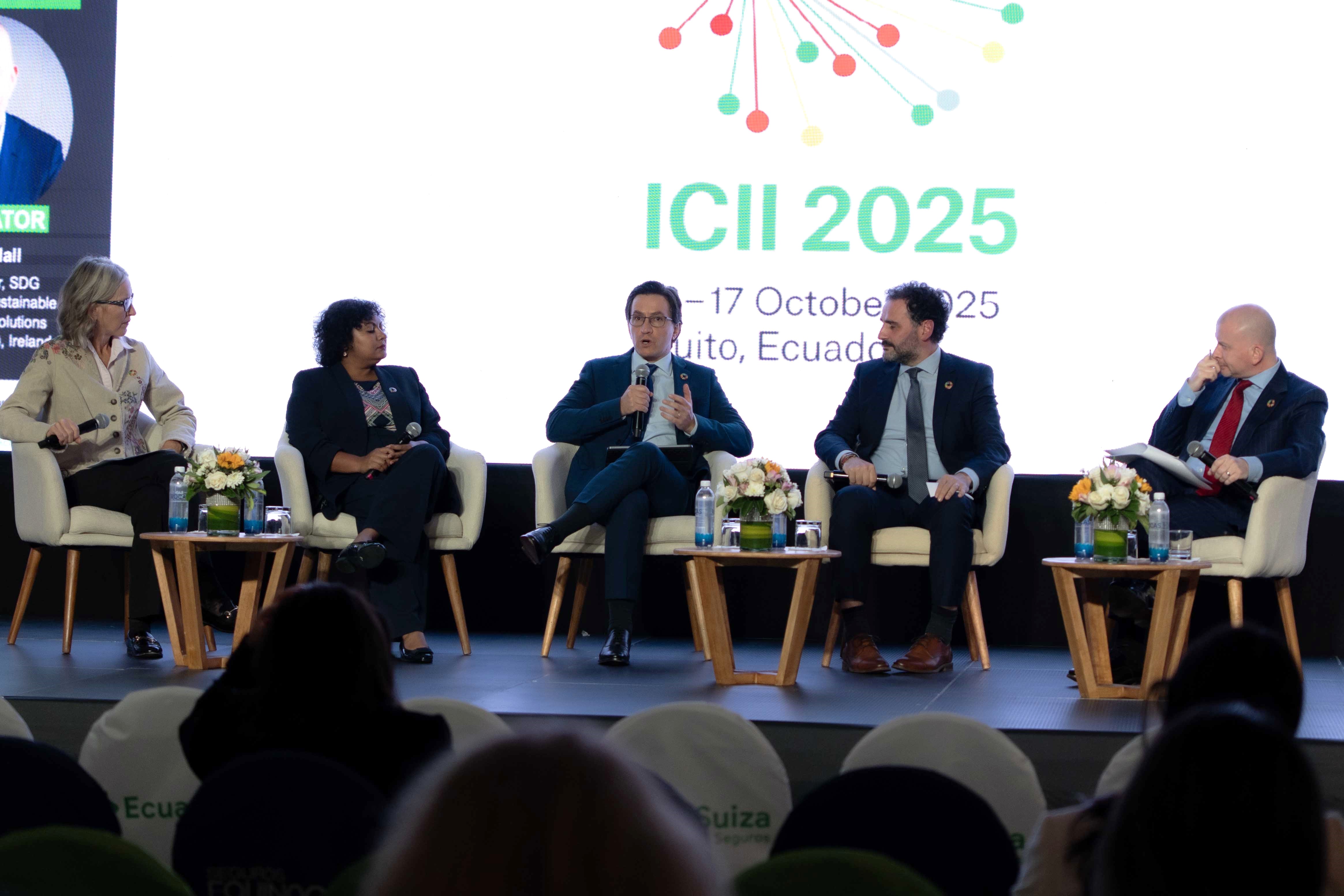 A panel discussion with five speakers seated on stage, with a large screen displaying "ICII 2025" in the background.