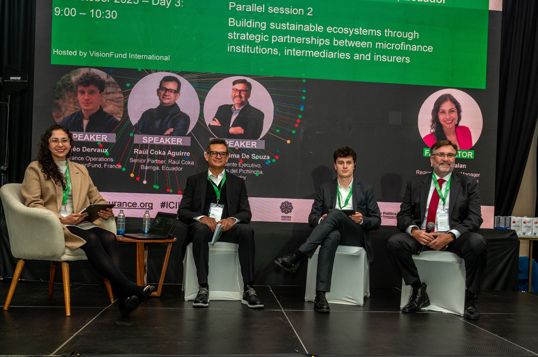 A panel discussion with four speakers seated on stage, with a presentation screen behind them.