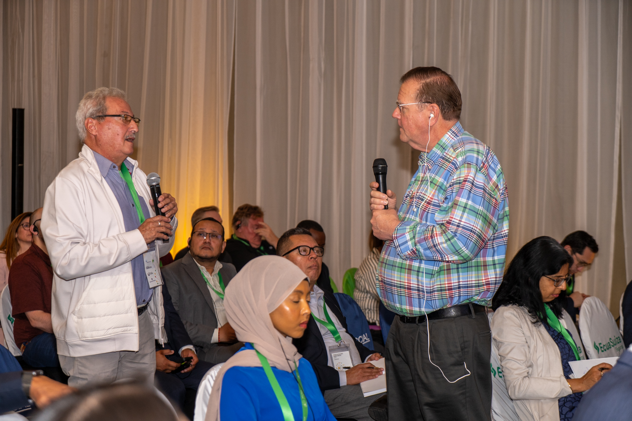 A speaker in a plaid shirt addresses an audience in a conference setting.