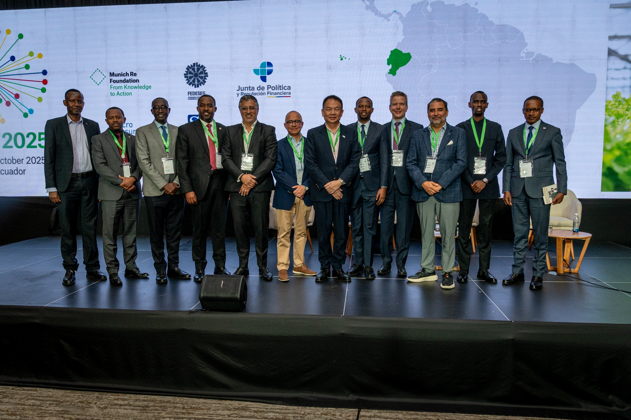 Group of men in formal attire standing on stage with a backdrop featuring logos and a map of South America.