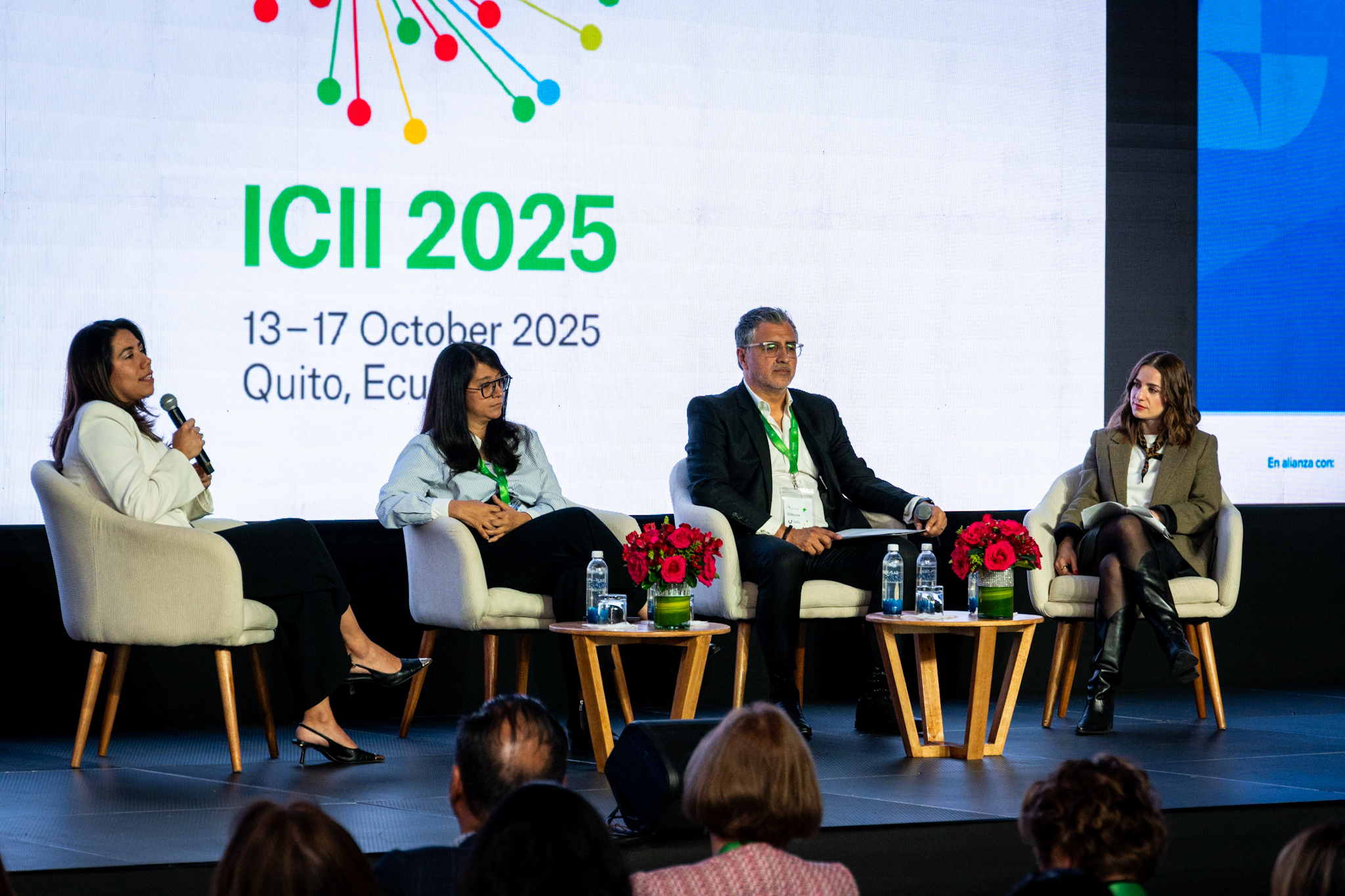Panel discussion at ICII 2025 event in Quito, Ecuador, featuring four speakers and a floral arrangement.