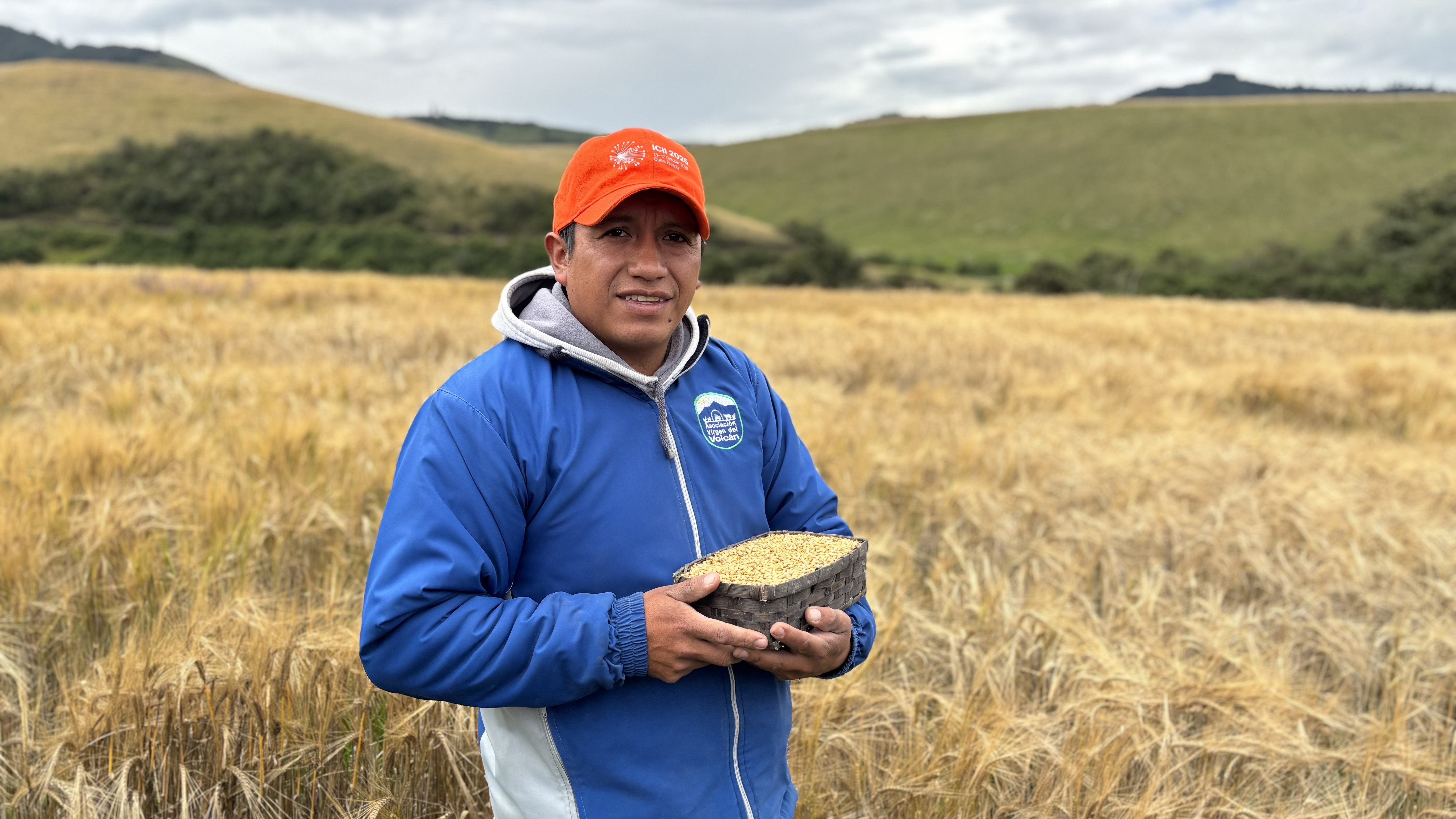 A large group of people in colorful hats poses outdoors in front of a building with a red roof and mountains in the background.