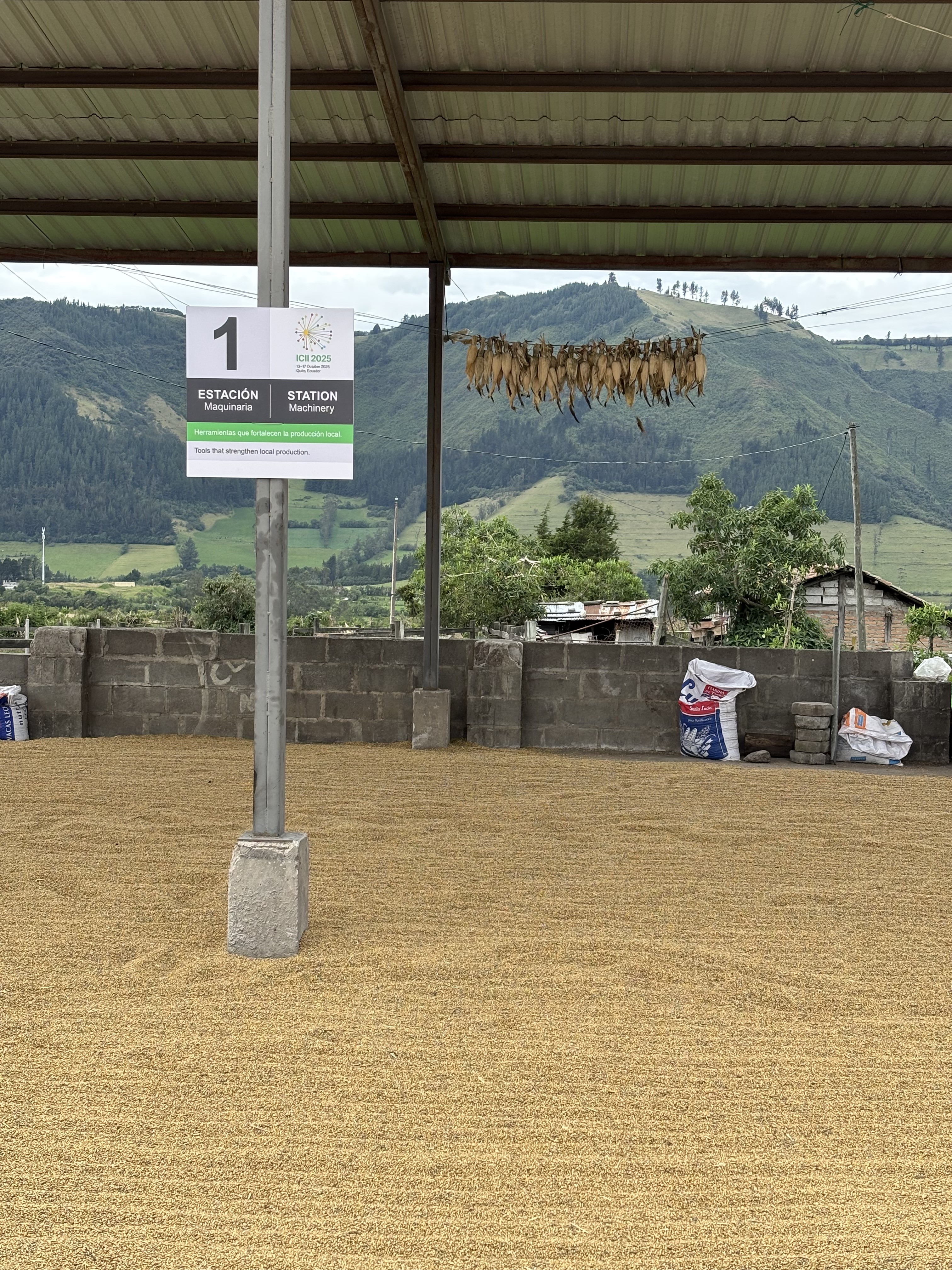 A covered area with a sign labeled "Estación Maquinaria" and dried produce hanging above, surrounded by mountains.