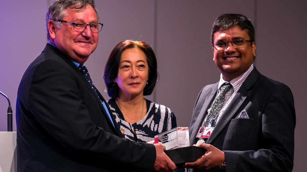 Thomas Loster (MRF) and Mami Mizutori, UN Special Representative of the Secretary-General for Disaster Risk Reduction, hand over the RISK Award trophy to Nandan Mukherjee (Dundee University) @UNDRR.
