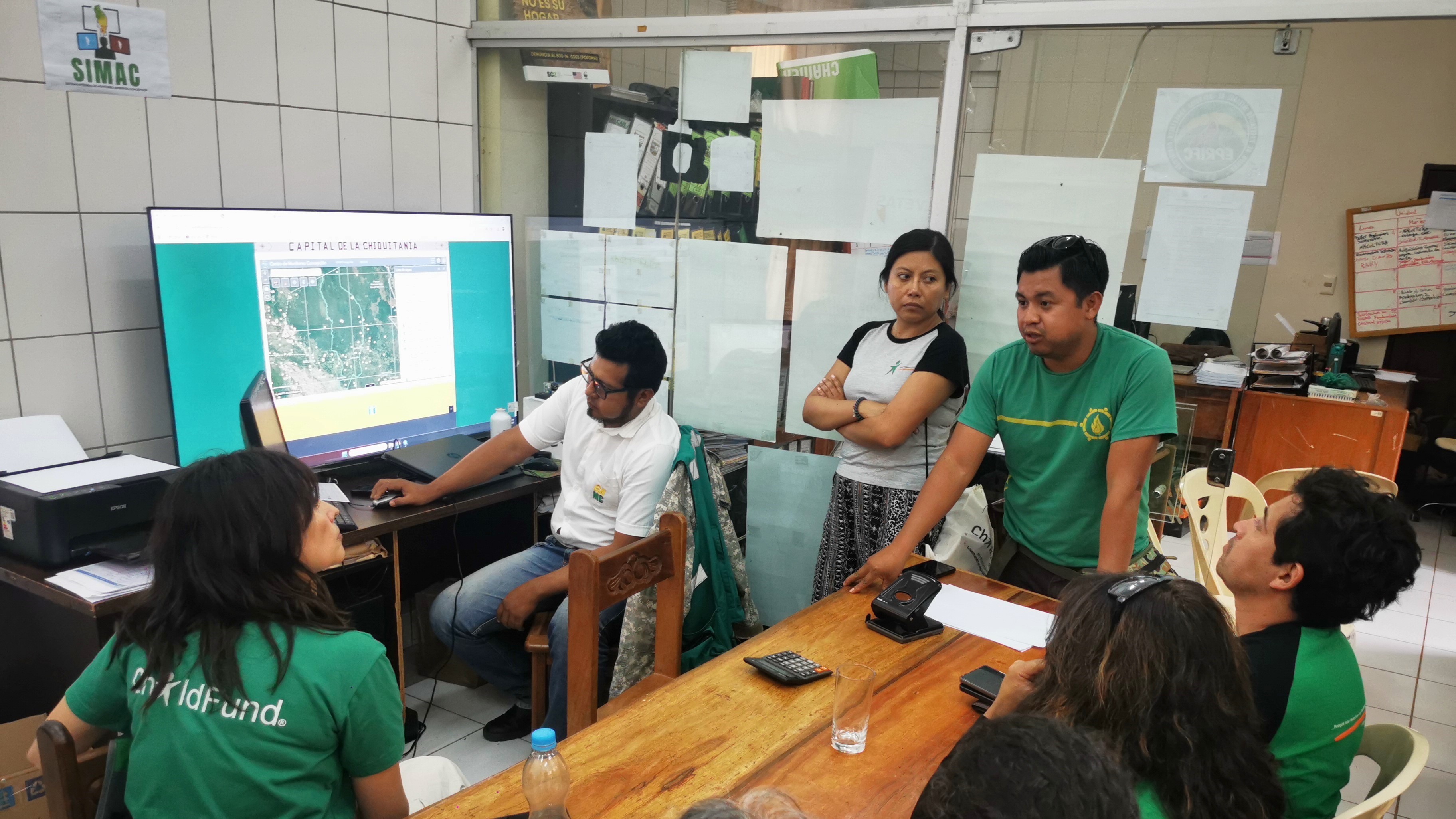 A group of people gathered around a computer screen displaying a map in an office setting.