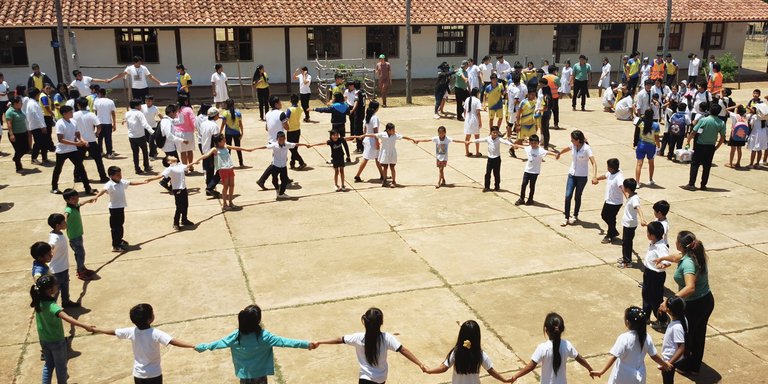 A group of children and adults participate in outdoor activities, forming a circle on a concrete playground.