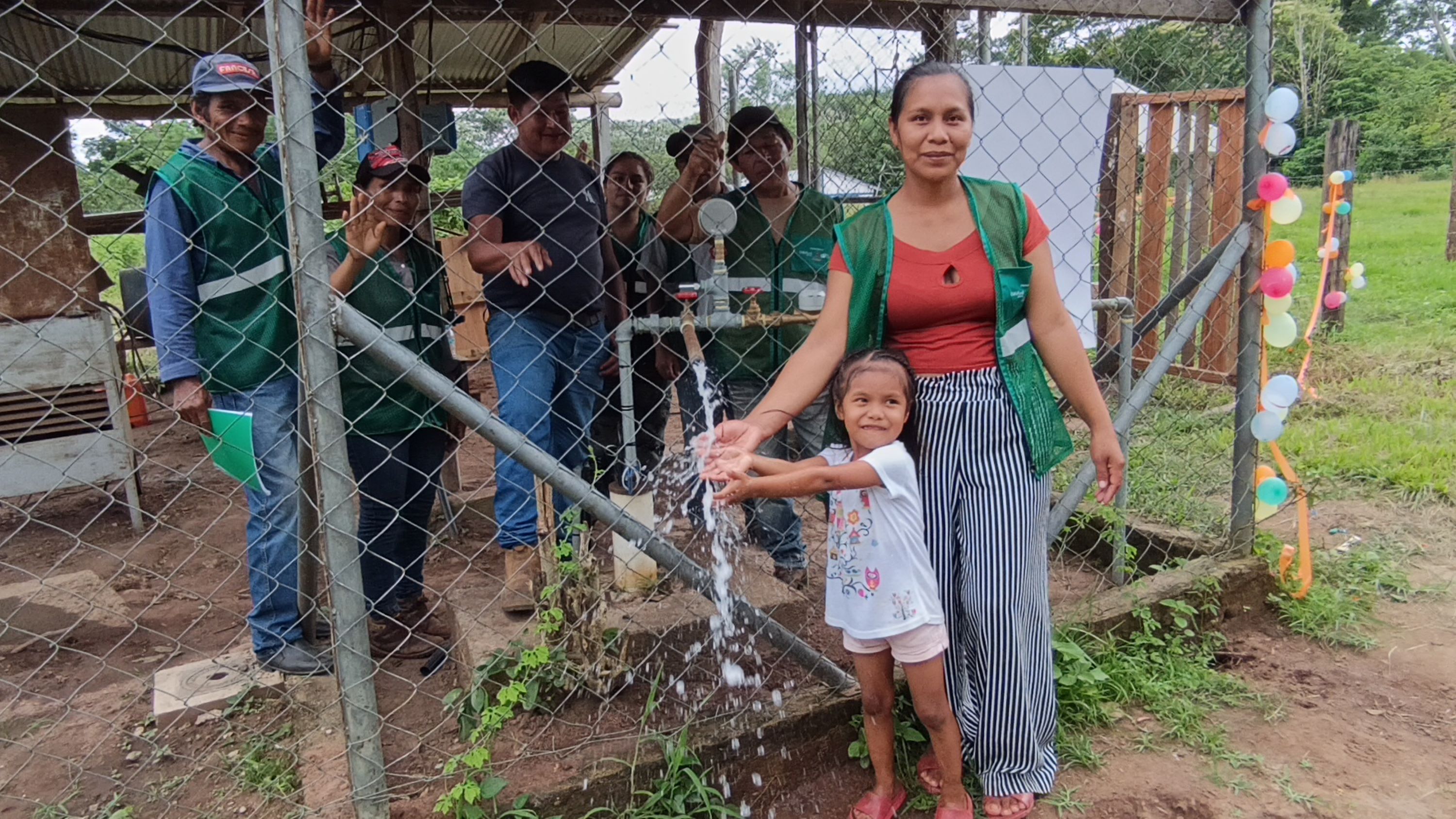 A woman and a child wash their hands at a water station, surrounded by several people in green vests.