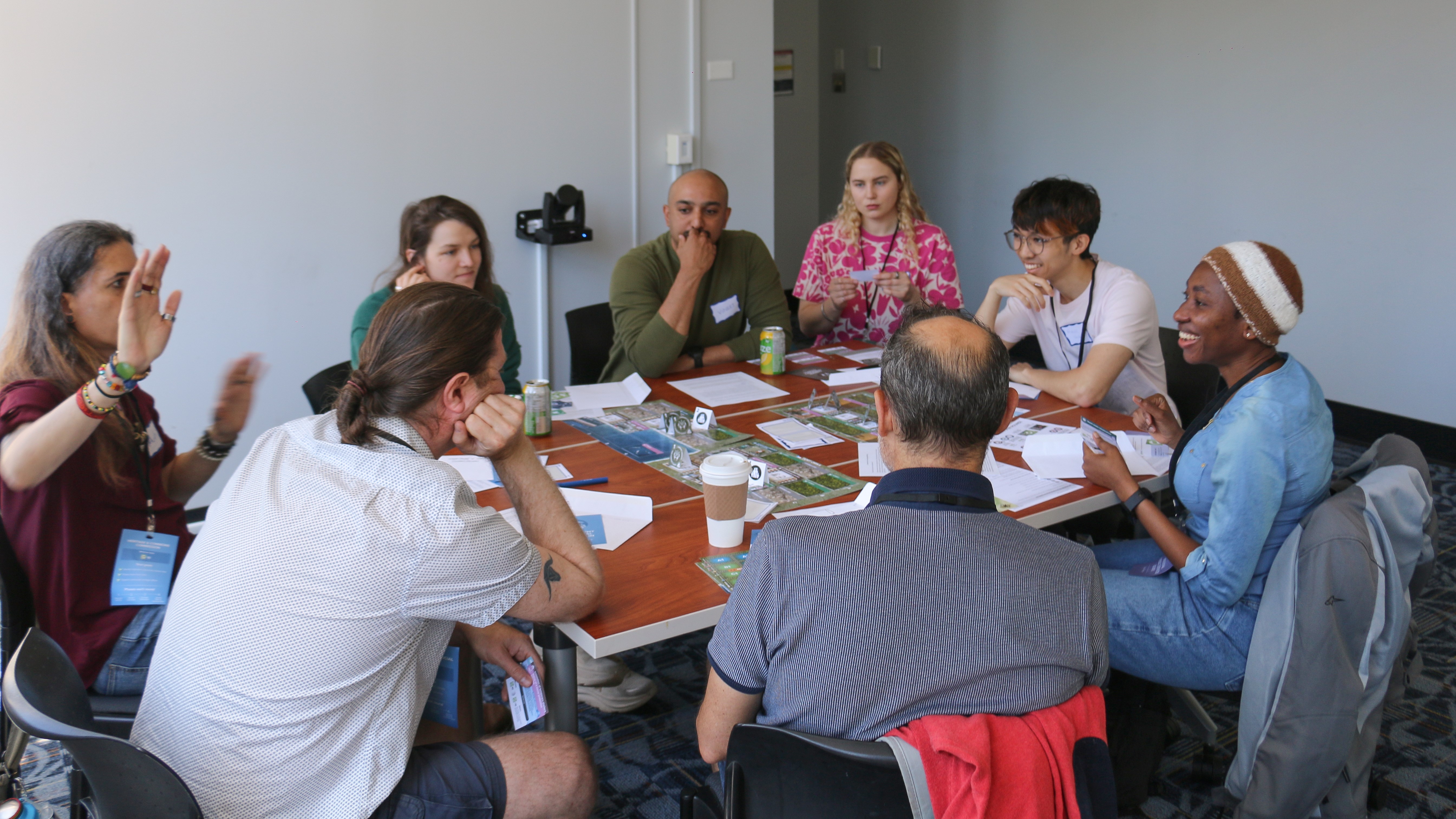 A group of people seated around a table engaged in discussion, with papers and drinks on the table.