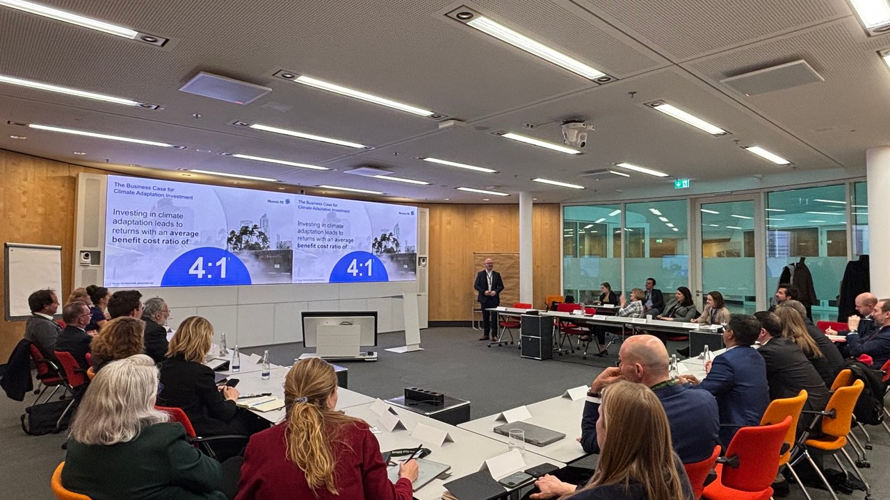 A conference room with a presentation on climate adaptation investment and attendees seated at tables.